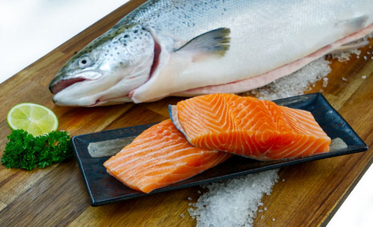 Salmon fillets on a plate with a whole salmon on a wooden surface.