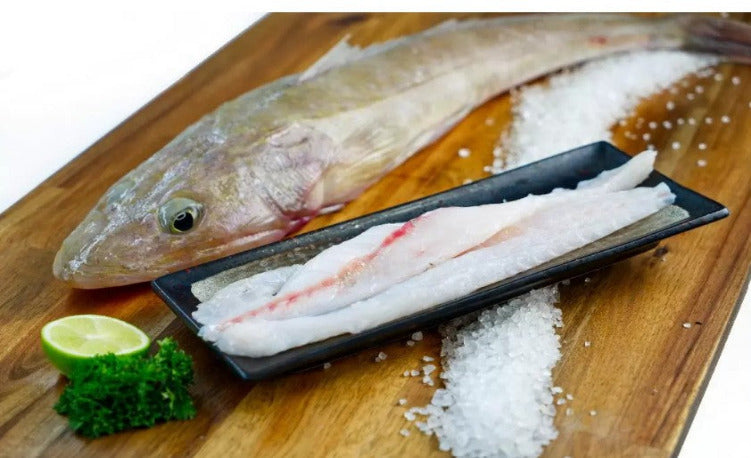 Flathead fillets on a black plate with a whole fish, salt, and a lime wedge on a wooden surface.