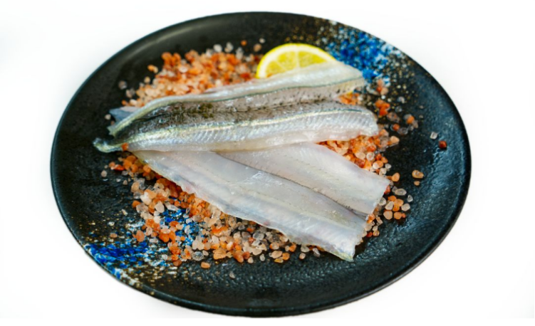 Garfish fillets on a bed of salt and pepper with a lemon wedge on a black plate.