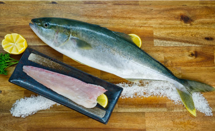 King Fish fillet and whole fish on a wooden cutting board with lemon wedges and salt.