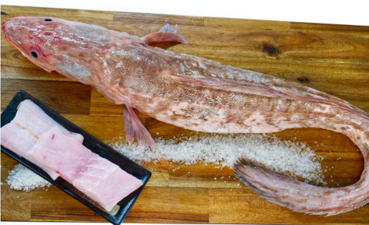 Ling fish on a wooden cutting board with salt and a black container of fillets.