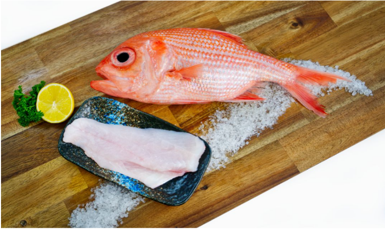 Red Snapper fillet and whole fish on a wooden cutting board with salt and lemon.