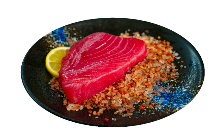 Raw tuna on a bed of salt and pepper with a lemon wedge on a black plate.